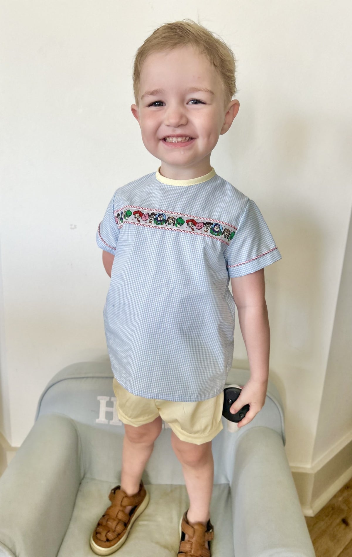 Boy wearing Easton Top in blue gingham with Toy Story ribbon, red piping and yellow bias neck